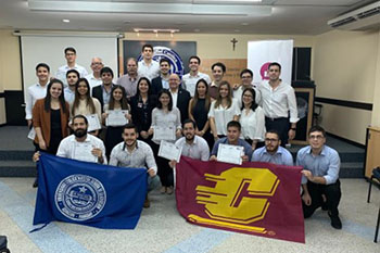 A group of Universidad Católica students, staff and CMU faculty Mike Pisani pose in a class room with a UC flag and CMU flag