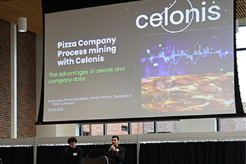 Two male CMU students presenting their case study in front of an audience during the Celonis Process Mining Competition.
