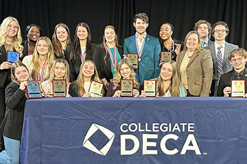 A group of students in business attire holding trophies from recent DECA competition.