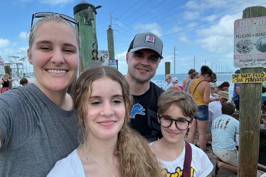 Aaron Draper poses in a hat with a Detroit Lions tshirt with his family - wife Katy in a gray tshirt, daughter keira with a necklace and white tshirt, son Eli in a white tshirt and black glasses - on a pier in Florida.
