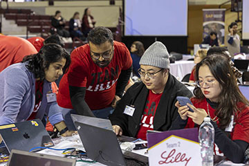 A group a students in red shirts gathered around computers competing in a business simulation.