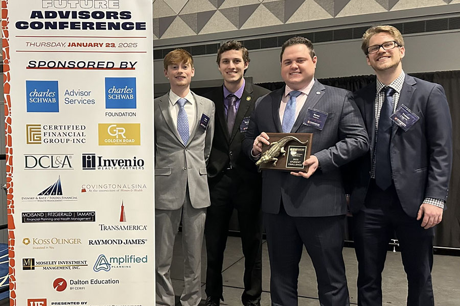 Four members of the finance program stand in business suits and hold a plaque after winning the FPA Challenge.