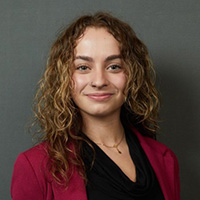 Savanna Stewart smiling in a professional headshot, wearing a maroon blazer against a dark background.