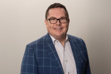 Bob Oros smiles in a studio headshot, wearing glasses, a blue plaid blazer and a light button-down shirt.
