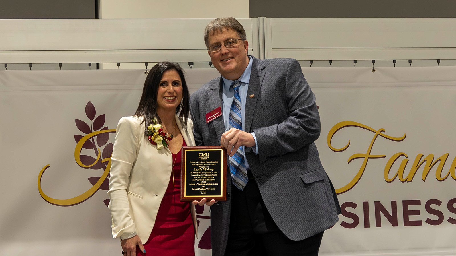 Leslie Vickrey receiving the CBA Hall of Fame Award. Standing next to her on stage in the Dean of the College of Business, Chris Moberg. They're posed on a stage in front of a CBA Hall of Fame banner.