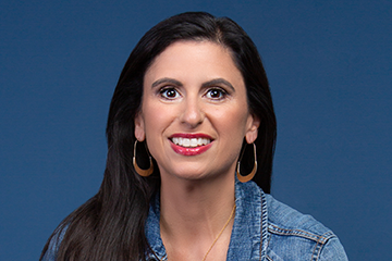 Professional headshot of Leslie Vickrey wearing a blue denim jacket in front of a blue background.