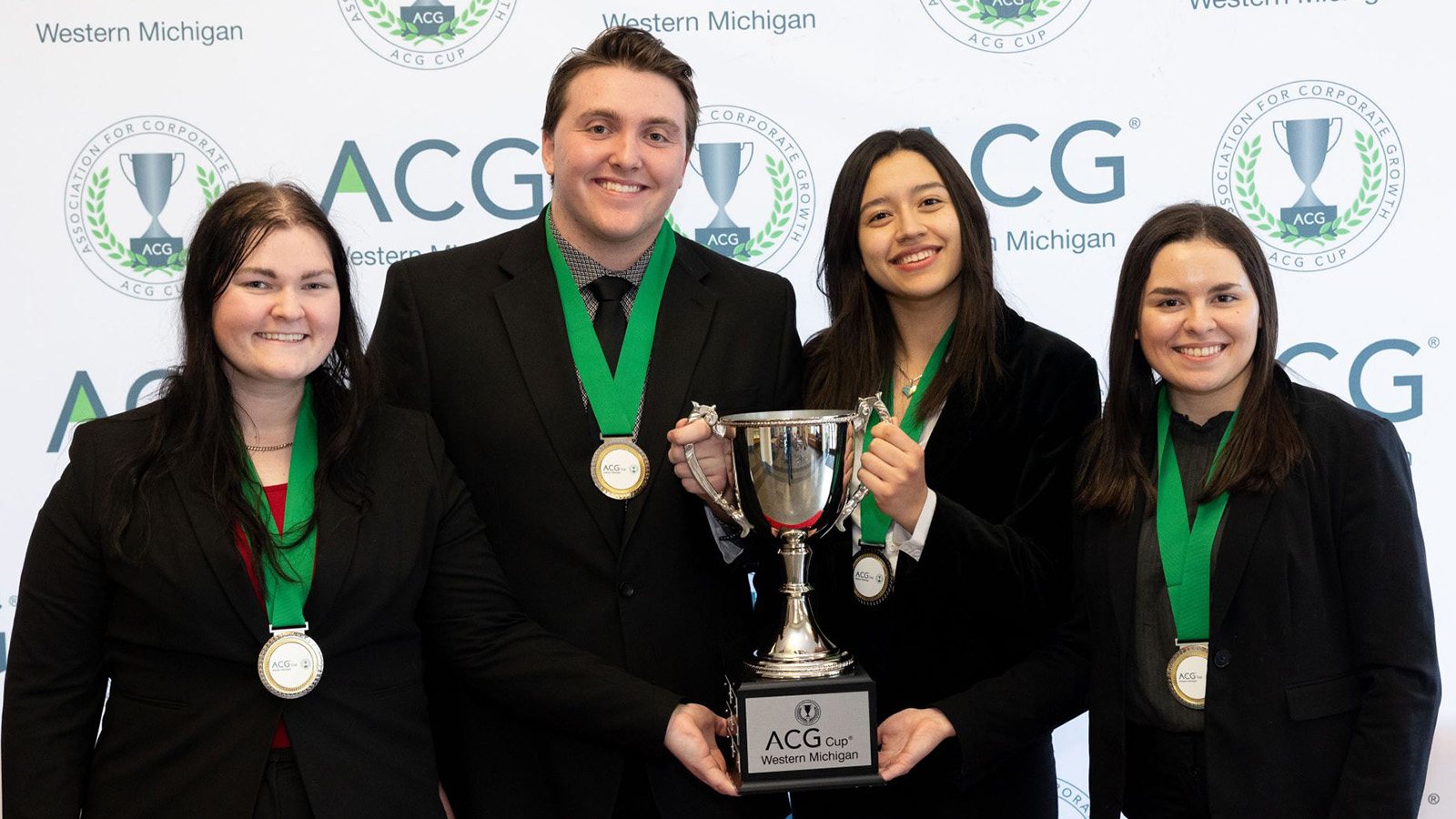 ACG Cup winning team (L to R) Lucy Forlastro, Jackson Raymond, Carolina Hernandez Ruiz and Corinne Sleeter. They are professionally dressed, wearing their new medals, and holding the ACG Cup in front of the ACG Banner.