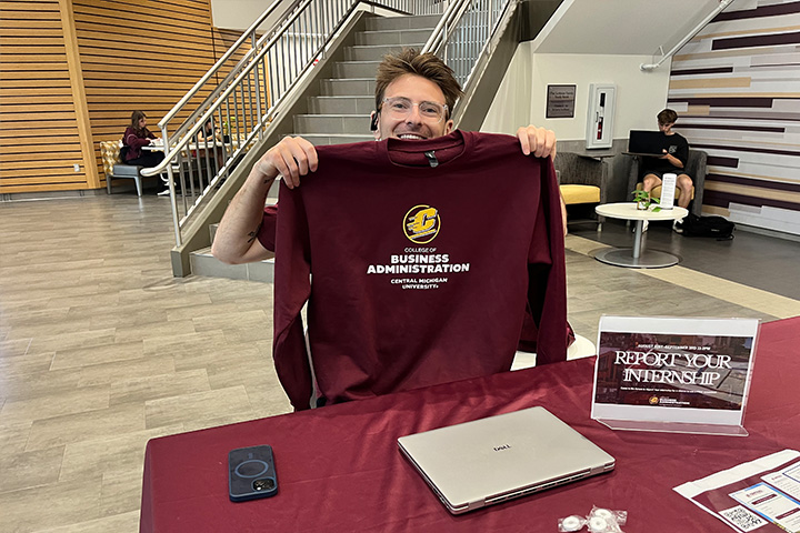 Anthony Niemiec holds a sweatshirt aloft as he poses and smiles for the camera. He's meeting students and asking about their summer internship experiences.
