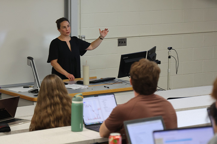 Professor Alexandra MacDougall is giving a lecture to students in her management class. She's in the front of the small auditorium class in Grawn.