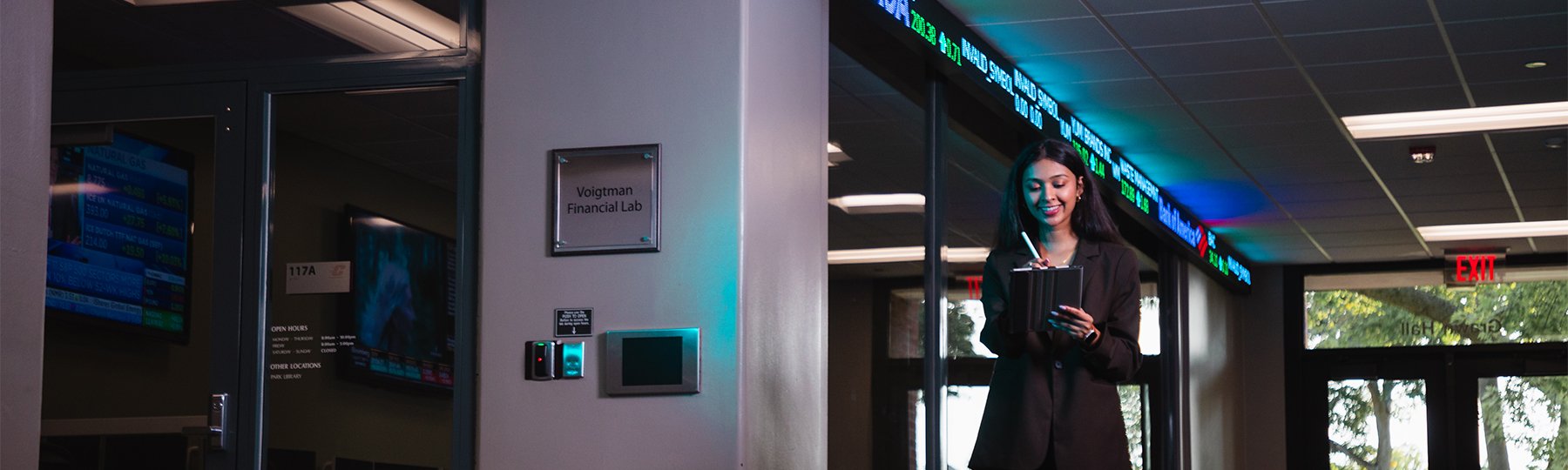 Female finance student writing on an iPad outside of the Voigtman Financial Bloomberg Lab.