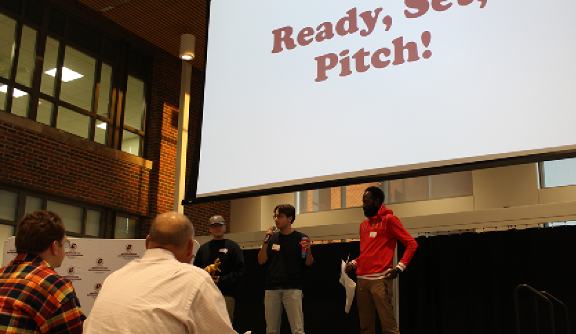 Three students on stage pitching their idea to a panel of judges in the Grawn Atrium