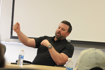 Jason St. John, a CMU alumni speaking to a class and talking with his arm raised.