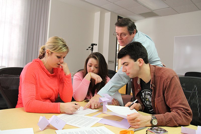 Lean Six Sigma Workshops with three students, two girls and one boy, sitting around a table working on a project with a professor providing feedback