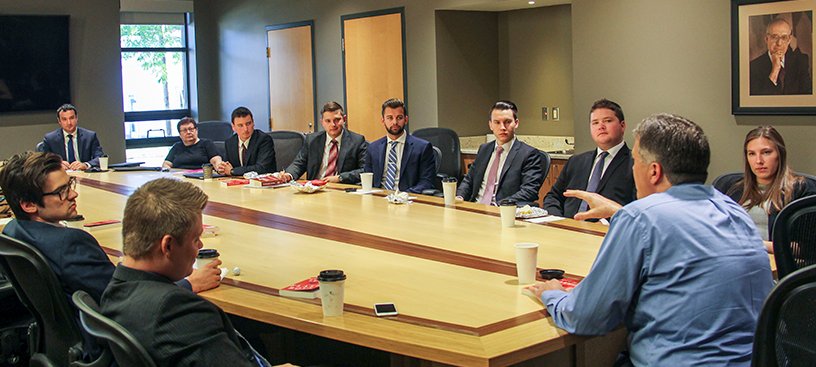 Michigan Finance Scholars meeting in Grawn Hall, men and women in suits sitting around a large conference table listening to a man speak