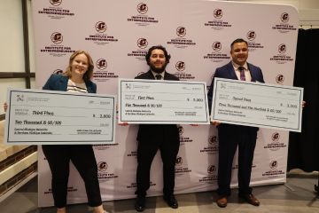A group of three students standing with their winning checks from the Michigan Collegiate Startup Challenge