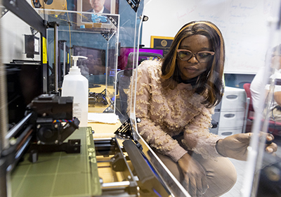 Female CMU student watching a 3D printer create a prototype in the IDEA Den.