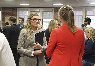 Female student holding a portfolio talking to a recruiter at a career fair.