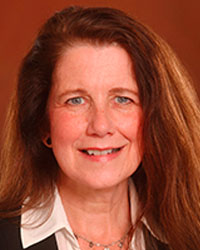 Lori Olsen has long brown hair and wears a white blouse in a professional headshot.