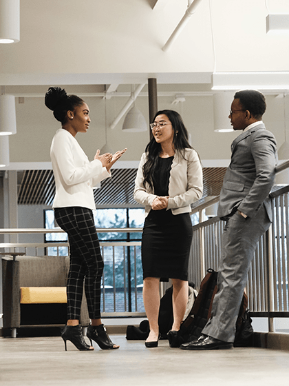 Three students in business attire standing and having a conversation.