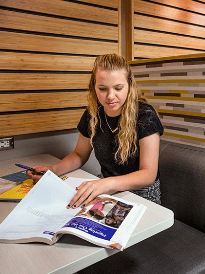 A student sitting down at a table and looking through a textbook.