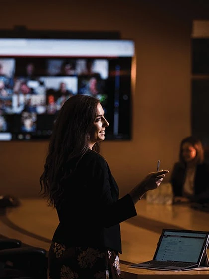 A woman standing and pointing in a meeting while talking.