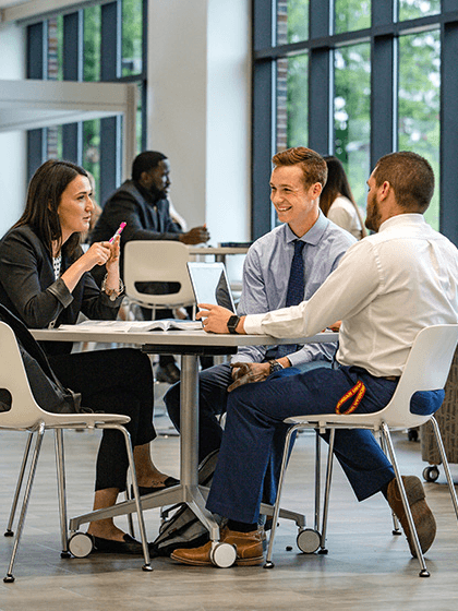 Three students wearing business professional clothing while sitting at a table and talking