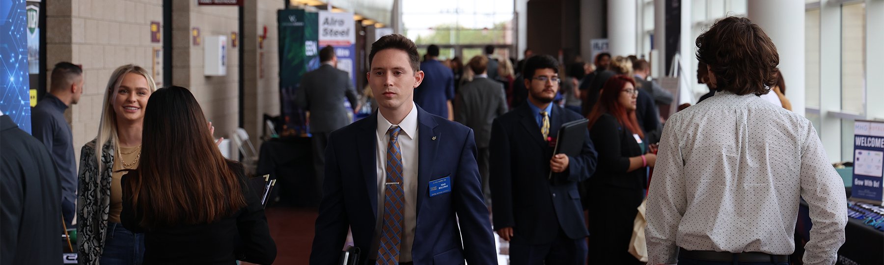 A male student in a blue blazer walking down the hallway during a career fair.