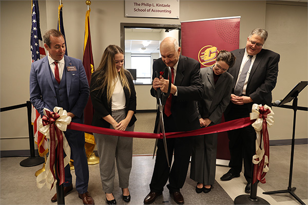 Philip Kintzele is flanked by CMU leadership as he cuts the ribbon in front of the newly appointed Philip L. Kintzele School of Accounting office in Grawn Hall. CMU President Neil MacKinnon and Dean Chris Moberg are in the picture.