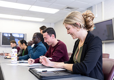 A small, diverse group of students are in a classroom. They are smiling and appear to be enjoying themselves.