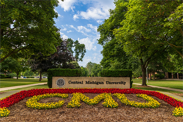 A photo of CMU's flower sign. The letters C-M-U are created using flowers. There's a permanent cement CMU sign behind them.