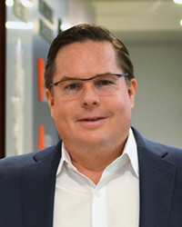 A man with glasses, wearing a white button up shirt and blazer.