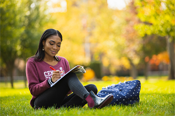 A student sitting on the grass writing in a book