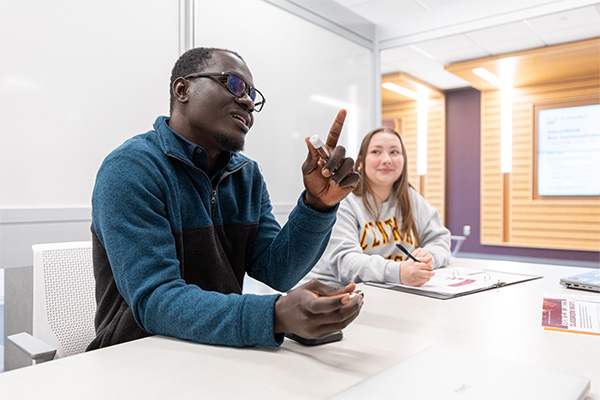 Two students are seen sitting at a study area table on Grawn's first floor. The student in the foreground has his finger raised as he leads the discussion, the student in the background is smiling and listening intently.