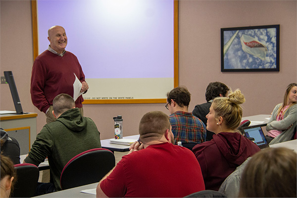 Dr. Tom Weirich can be seen smiling in the background of this photo as he gives a lecture to his accounting class.