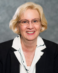 a professional headshot of Candace Gibsonn who has blonde hair, wears glasses and is wearing a white collared shirt underneath a black blazer.