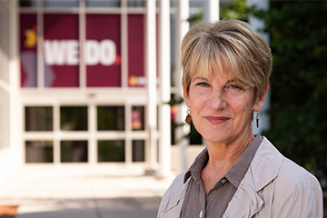 Woman with short blonde hair smiles at the camera in front of a university building.