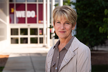 Alison Arnold in front of the College of Medicine building with the We Do banner in the background.