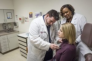 Man in a white lab coat places stethoscope on a woman's heart.