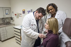 Man in a white lab coat places stethoscope on a woman's chest.