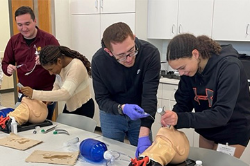 Two female students practice intubation on a mannequin head while two male instructors assist.