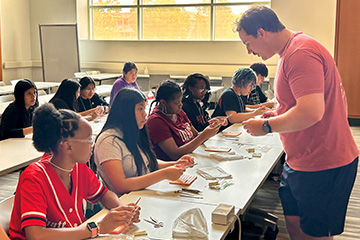 A medical student teaches a group of high schoolers how to suture on practice kits.
