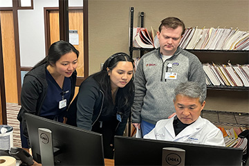 Two female and one male student look over the shoulder of a doctor viewing computer monitors.