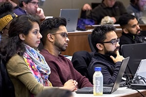 Three medical students, two males and one female, sit at a desk and face forward in a lecture hall.