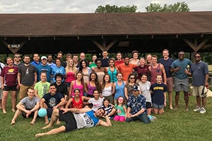 A large group of students gather together and smile for a picture outside in front of a pavilion at the End of the Year Picnic.