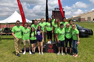 A group of young adults wearing lime green shirts stand together and smile at a Michigan summer special Olympics event.