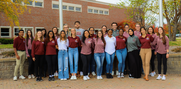 A group of student Dean's Ambassadors wearing matching polos stand together and smile.