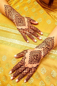 Hands with henna tattoos lying on a table with yellow tablecloth.