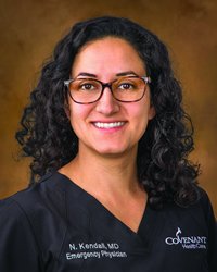 A woman with dark hair and glasses wears a dark blue medical scrub shirt