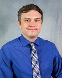 Professional headshot of Michael Opperman wearing a blue collared shirt with striped tie