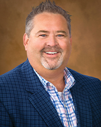 a man smiling in a blue plaid suit in front of a dark yellow background